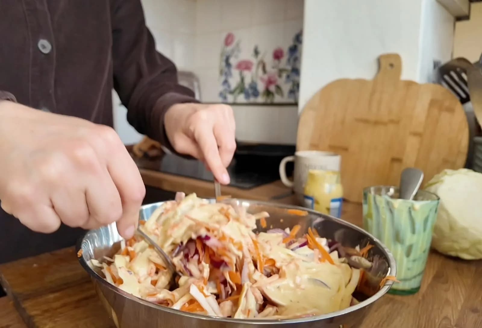 Person using two utensils to mix slaw with dressing in a large bowl.