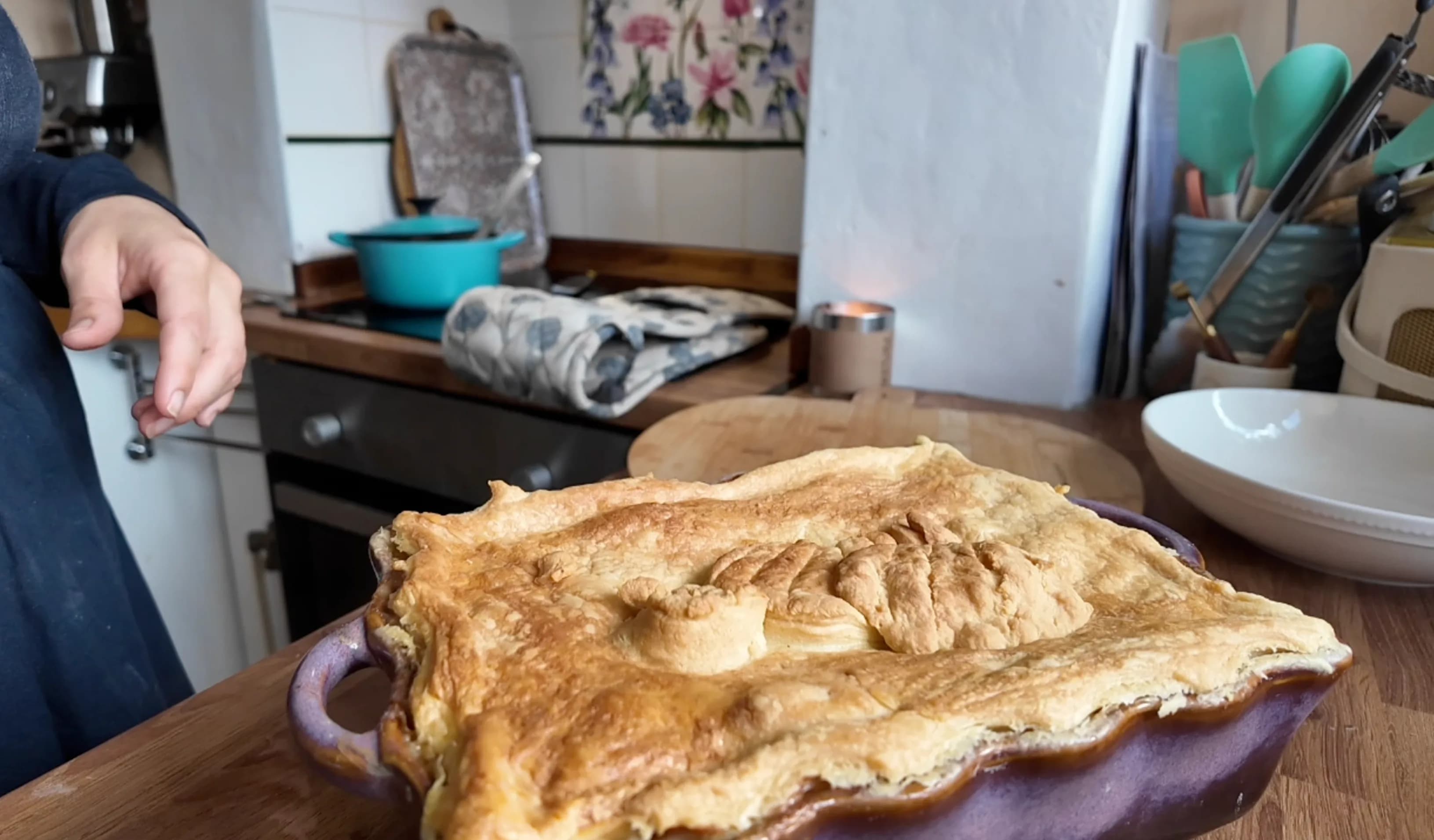 A baked chicken pie in a purple dish with golden brown puff pastry on top.