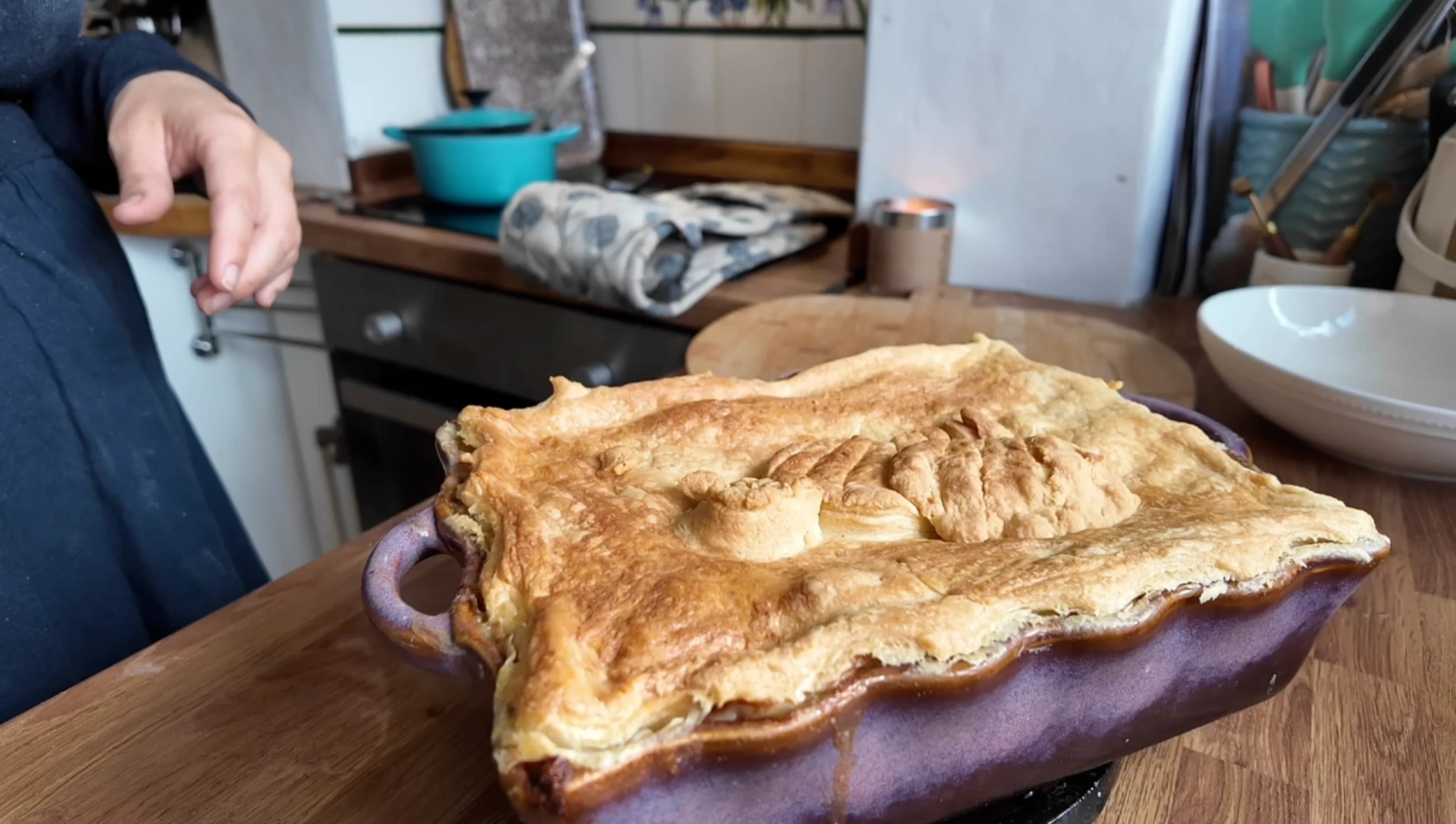 A baked chicken pie in a purple casserole dish with a golden puff pastry crust.
