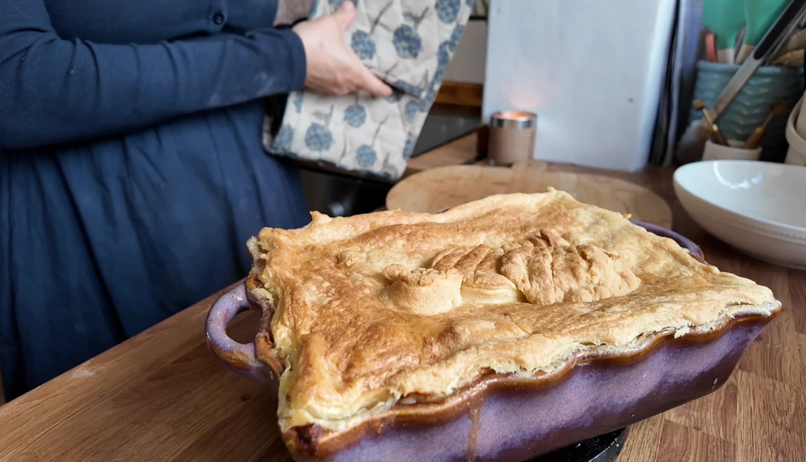 Close-up of a chicken pie in a purple dish with a golden puff pastry lid.
