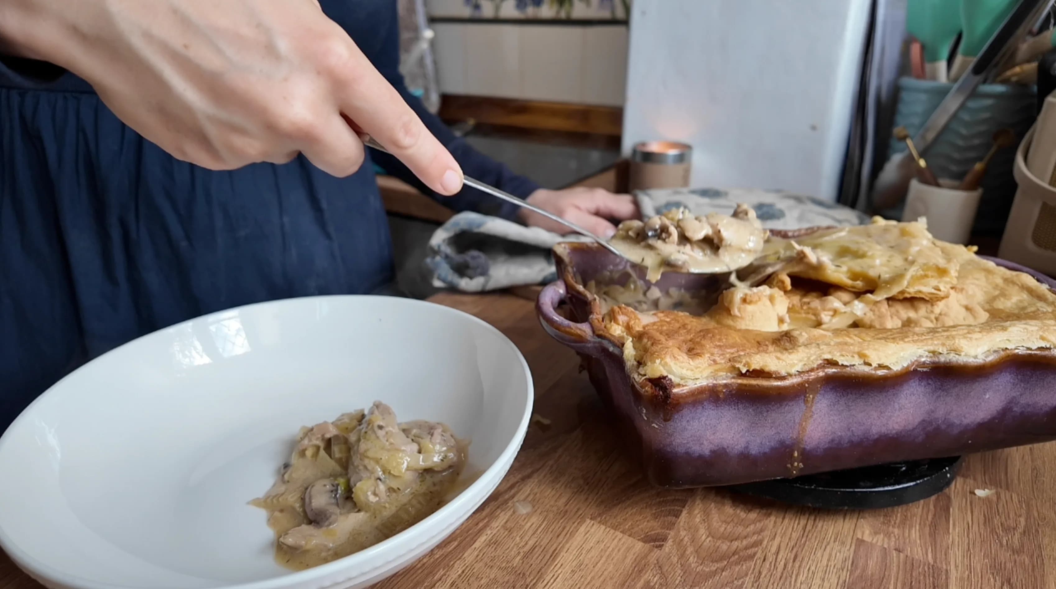 A person serving chicken pie with a spoon from a purple dish onto a plate.
