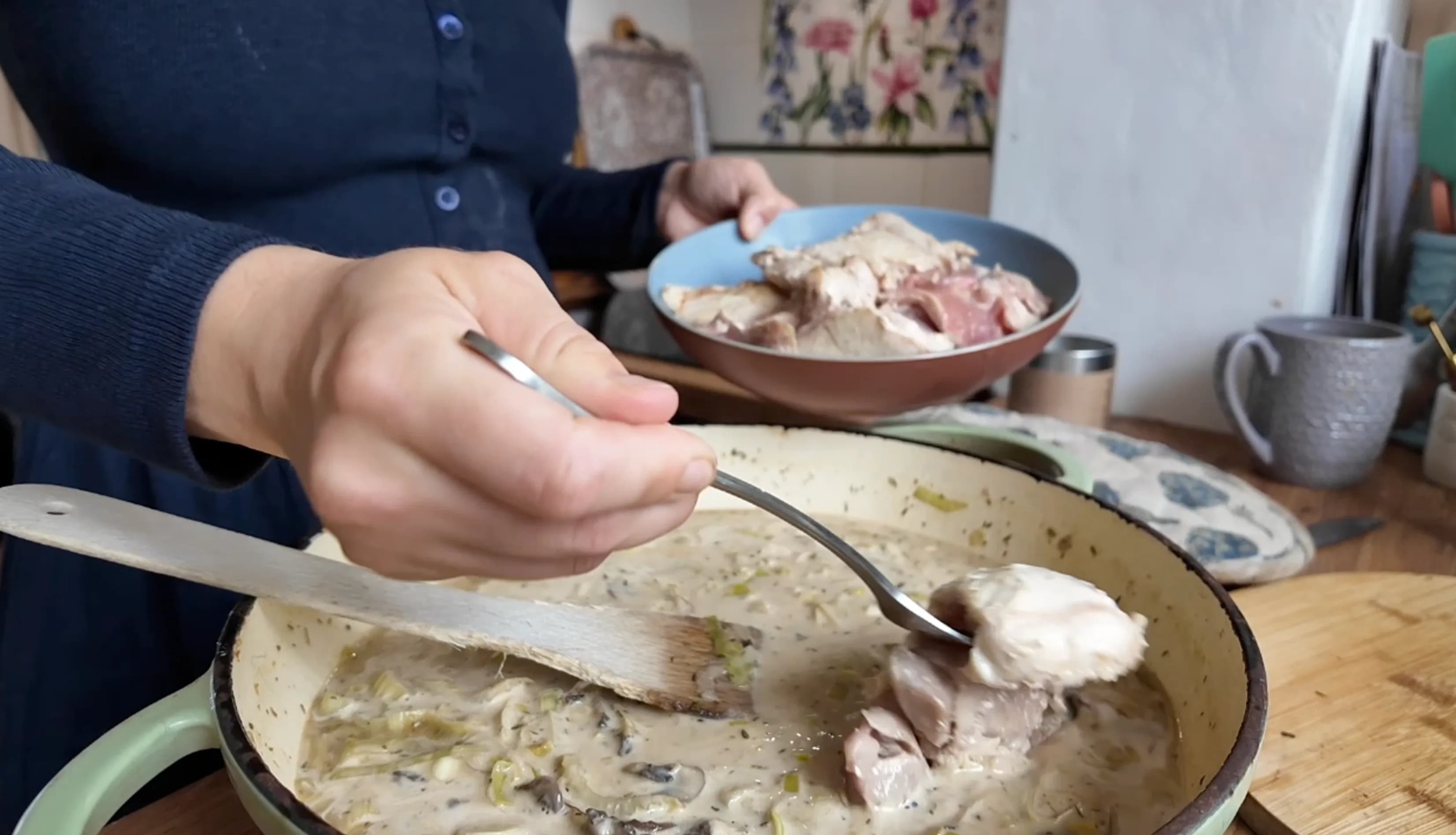 A person adding pieces of chicken into a pan with sauce.