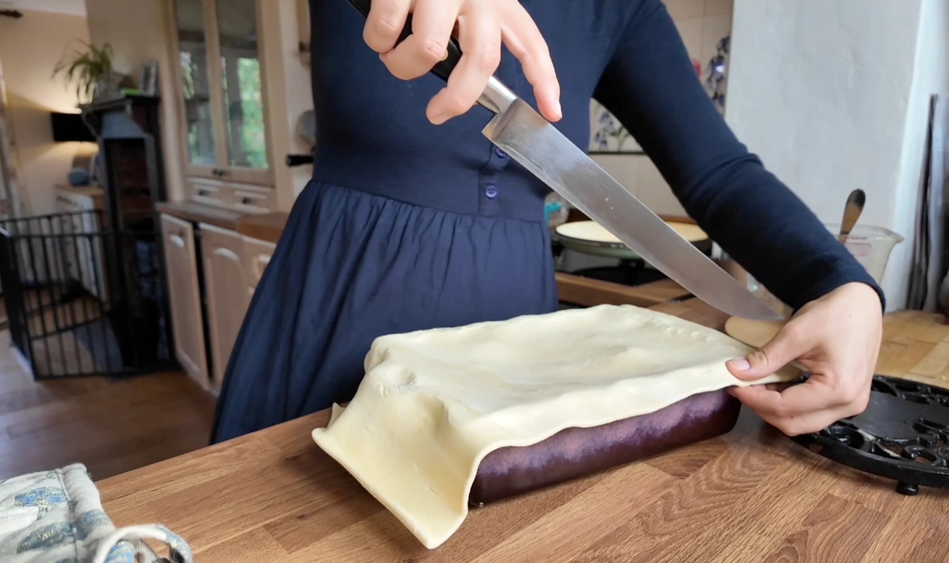 Person trimming excess puff pastry from a pie dish with a knife.